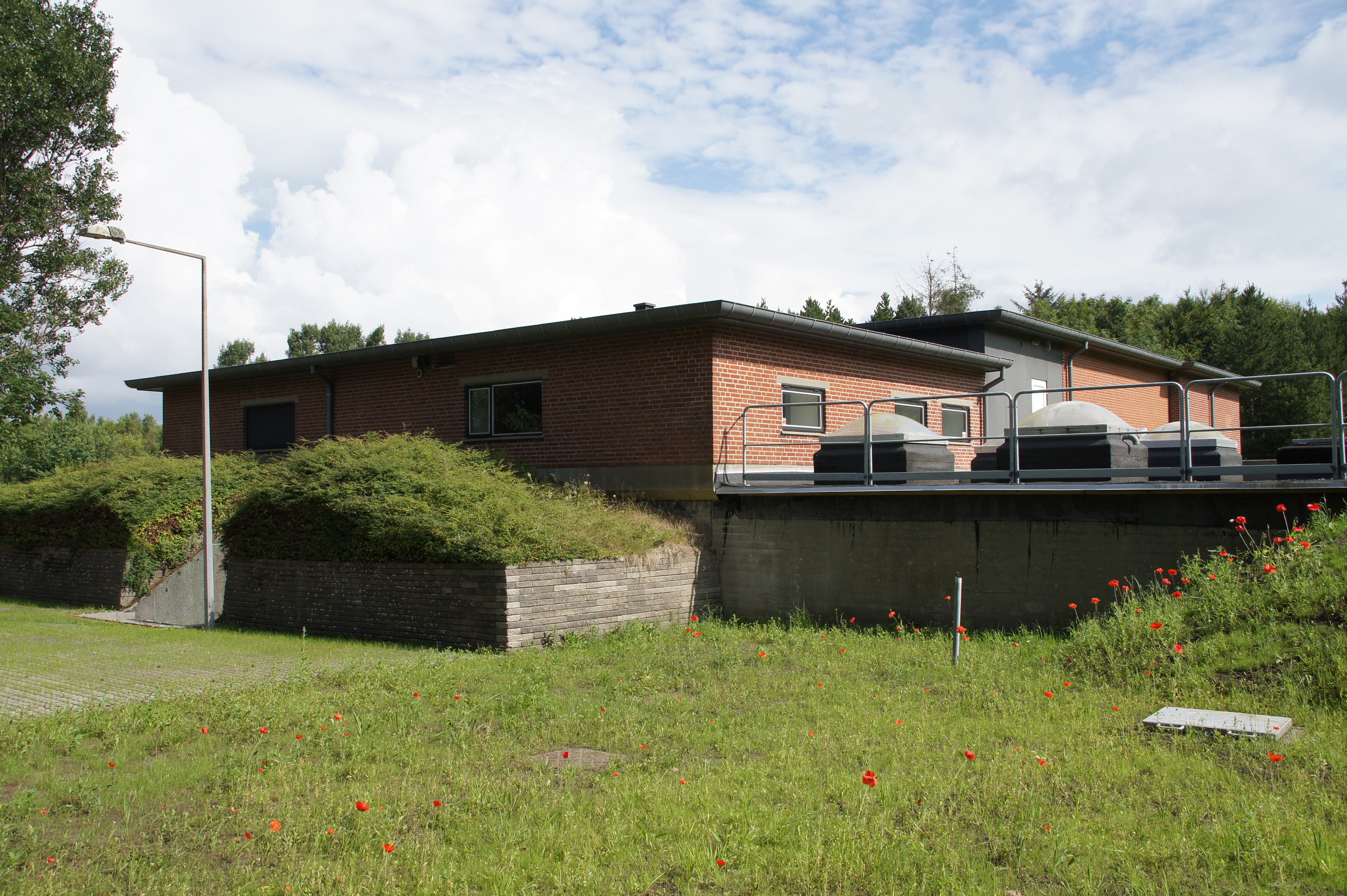 Vester Gjesing Vandværk - Rød bygning med bevoksning foran.
